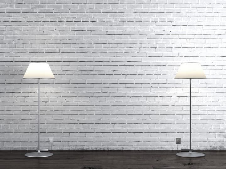 Two modern floor lamps illuminate a white brick wall in a minimalist setting.