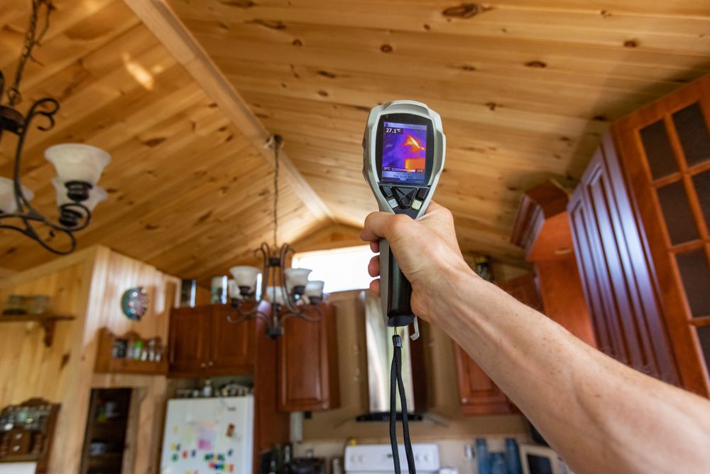 Hand holding a thermal imaging device in a wooden ceiling room.