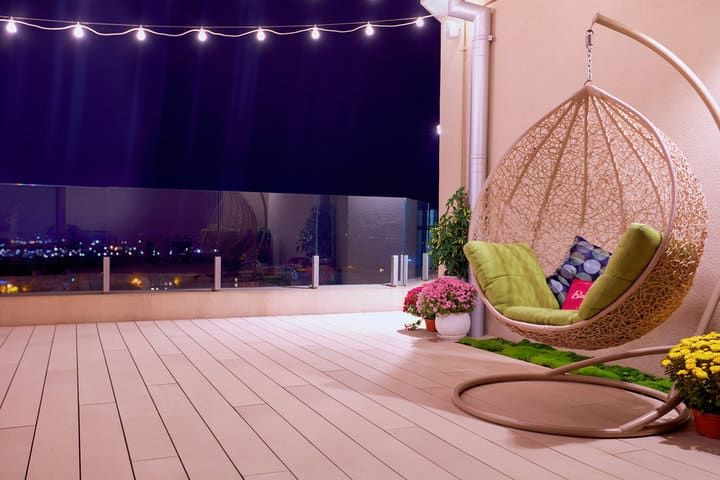 Cozy balcony with a hanging chair, flowers, and string lights at night.