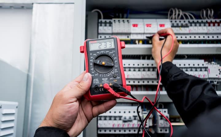 A person using a multimeter to test electrical connections in a control panel.