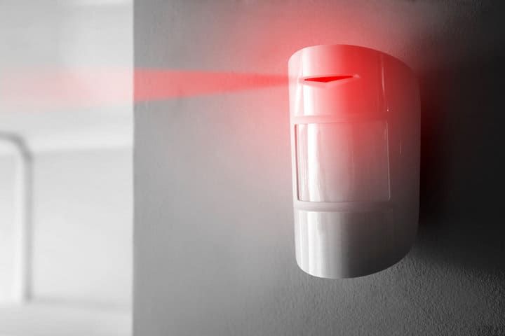 A white motion sensor emitting a red beam on a wall.