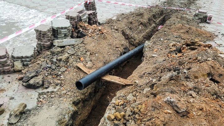 Excavated trench with a black pipe across the bottom and surrounding dirt.
