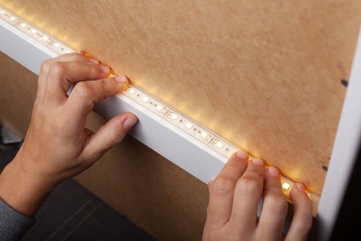 Hands installing LED strip lights onto a wooden surface.
