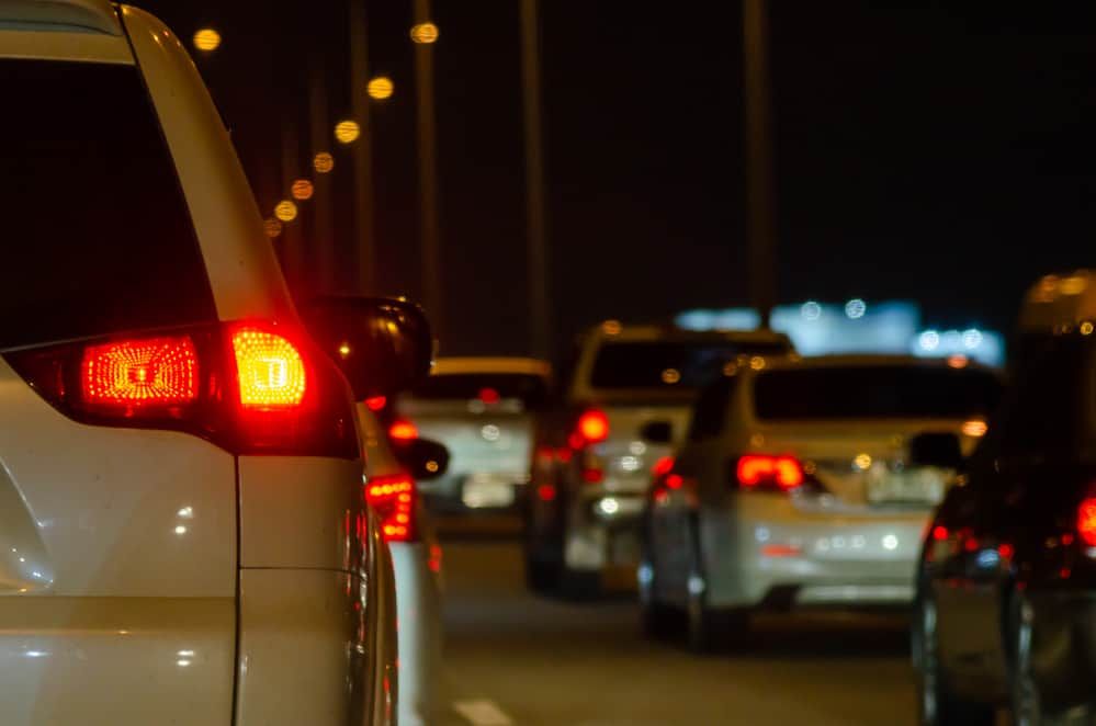 A line of cars with red brake lights glowing in the dark.