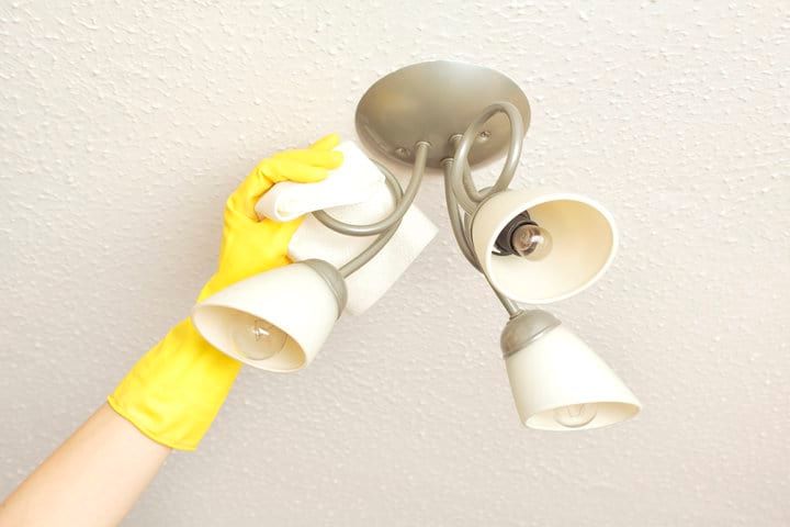 A hand in a yellow glove cleaning a ceiling light fixture.