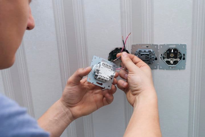 Person installing an LED light switch onto a wall with exposed wiring.