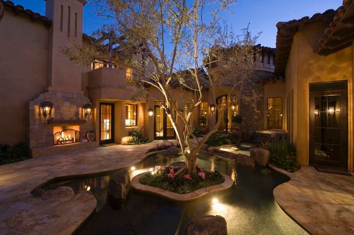 A beautifully lit courtyard featuring a tree, flowers, and warm outdoor lighting.