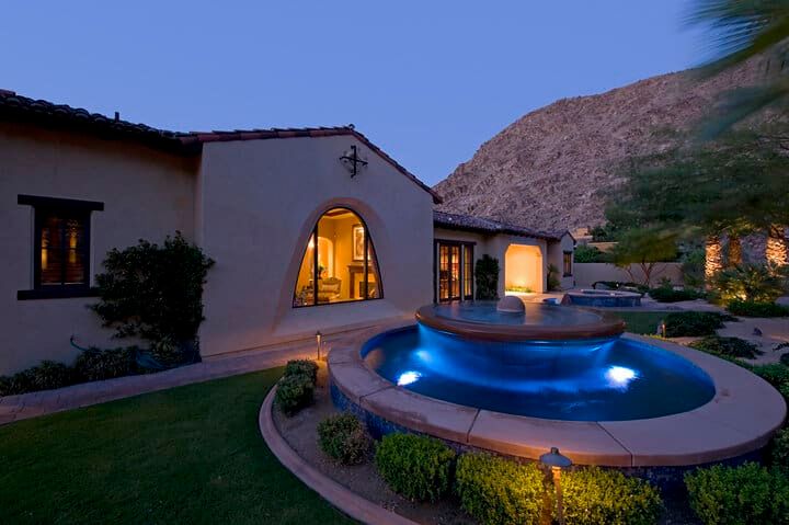 A beautifully lit backyard with a fountain surrounded by greenery and mountains.