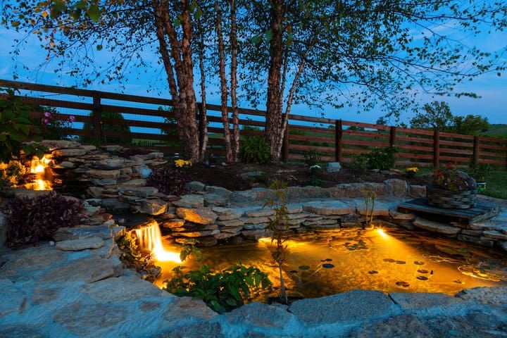 A serene pond with stone features illuminated by warm LED lights at dusk.