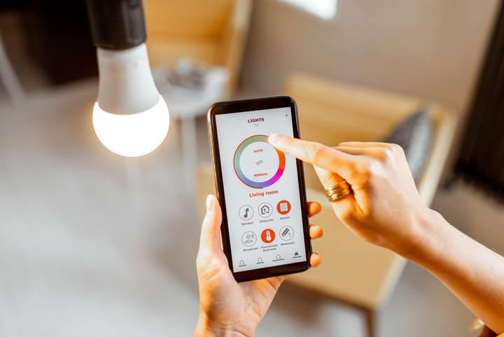 A person adjusting smart LED lighting using a smartphone app with a glowing bulb above.