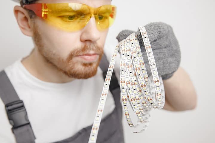 A worker examines multiple reels of LED lighting strips closely.