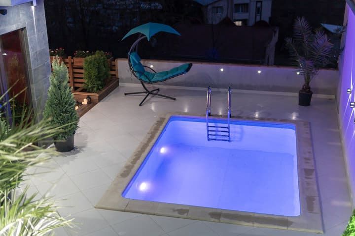 A serene swimming pool illuminated with blue LED lights, surrounded by greenery.