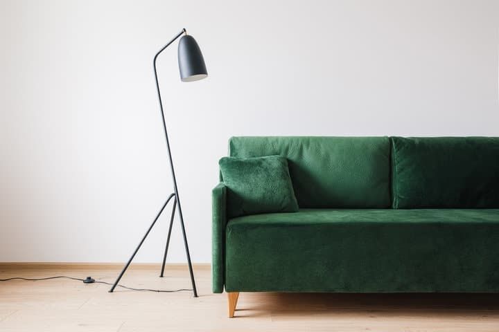 A modern green sofa beside a stylish floor lamp in a minimalist setting.