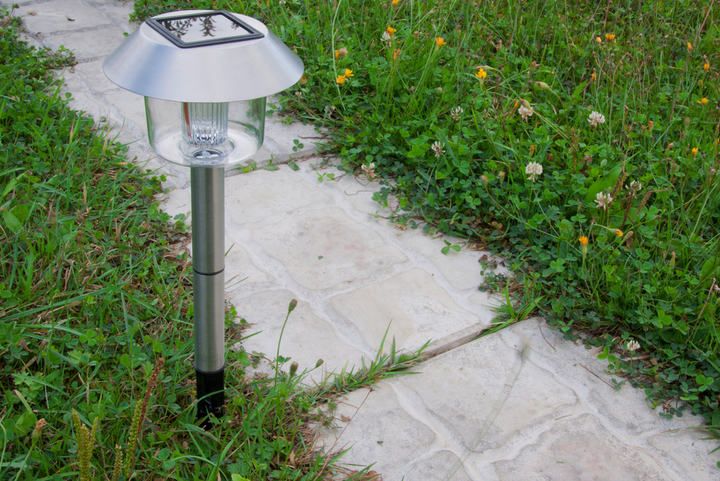A solar-powered LED garden light stands beside a stone pathway in grass.