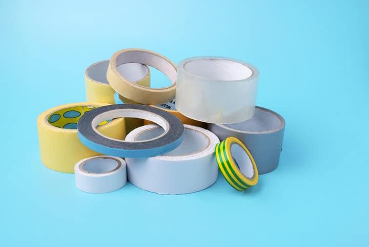 Various rolls of masking tape in different colors and sizes on a blue background.