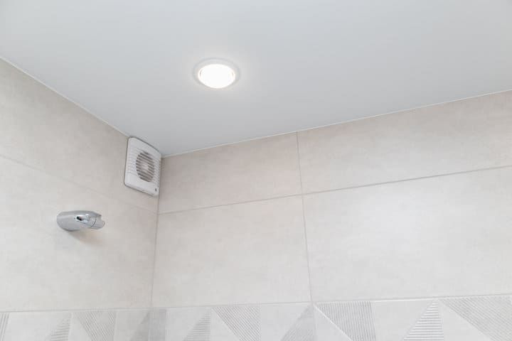 Recessed LED light fixture installed in a bathroom ceiling with tiled walls.