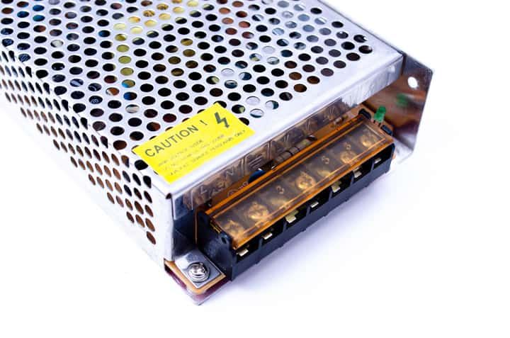 Metallic LED driver power supply with warning label and connection terminals.