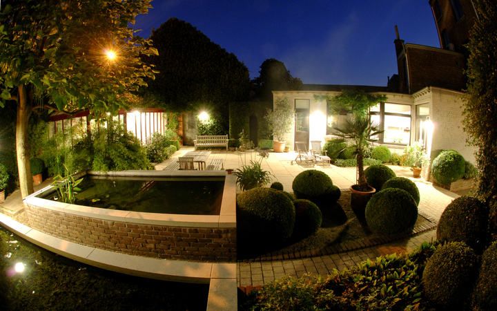 A beautifully lit garden at dusk with a pond and seating area.