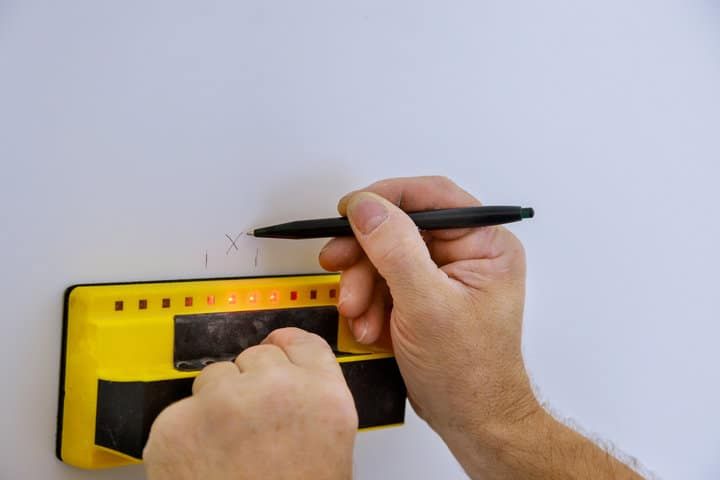 Hands using a level tool to mark positions on a wall.