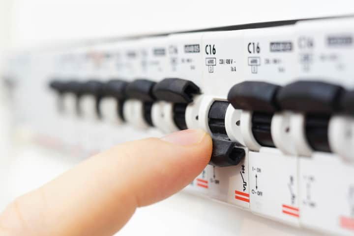A finger is pressing a circuit breaker switch on a control panel.