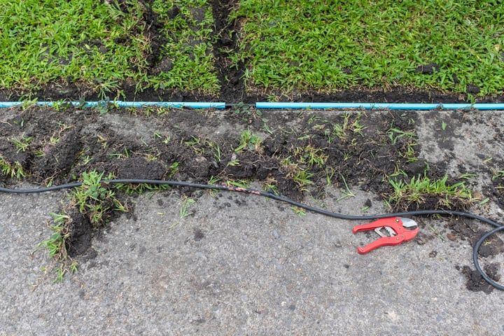 A red clip lies on uneven ground with green grass and exposed wiring.