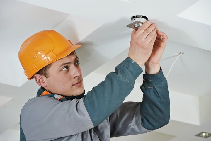 A worker installing an LED light fixture in a ceiling.