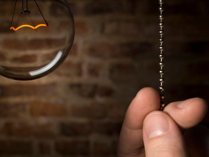 A hand pulls a chain to turn on a vintage LED bulb.