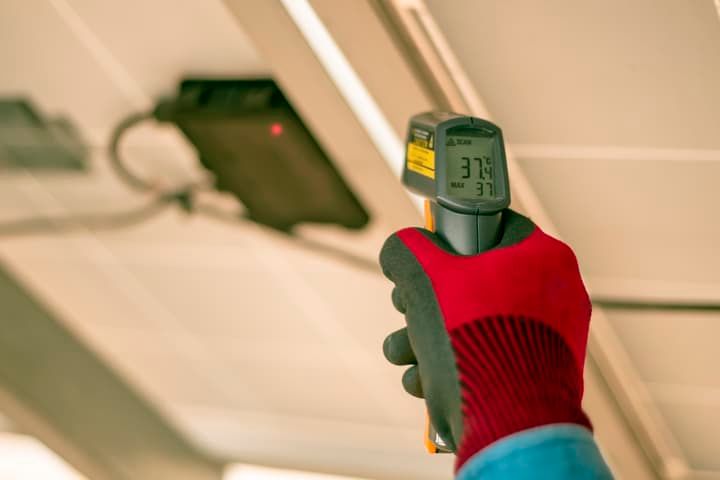 Hands wearing red gloves use an infrared thermometer to measure surface temperature.