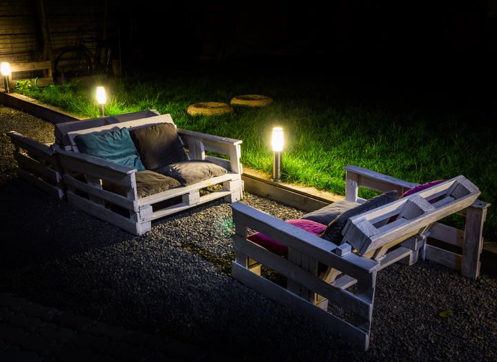 Two pallet sofas with cushions and soft LED lights in a garden at night.