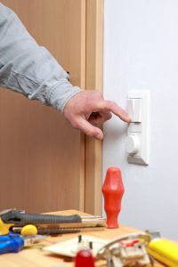 A hand adjusting a light dimmer switch with tools on a table nearby.