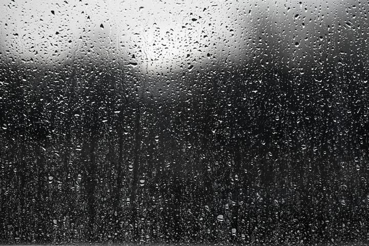 Close-up of water droplets on a window with a blurred background.