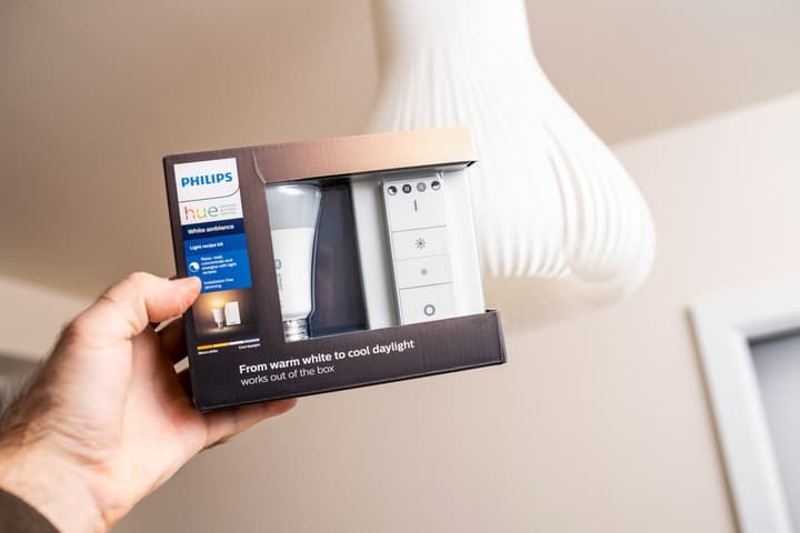A hand holding a Philips Hue LED light and remote control package.