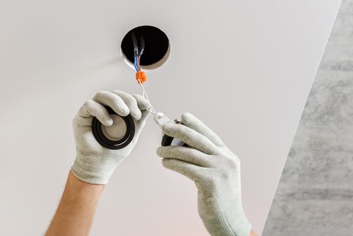 A person installing an LED light fixture in a ceiling opening.