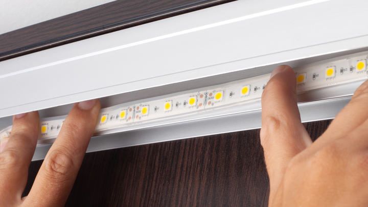 Two hands installing LED strip lights into a mounting track.