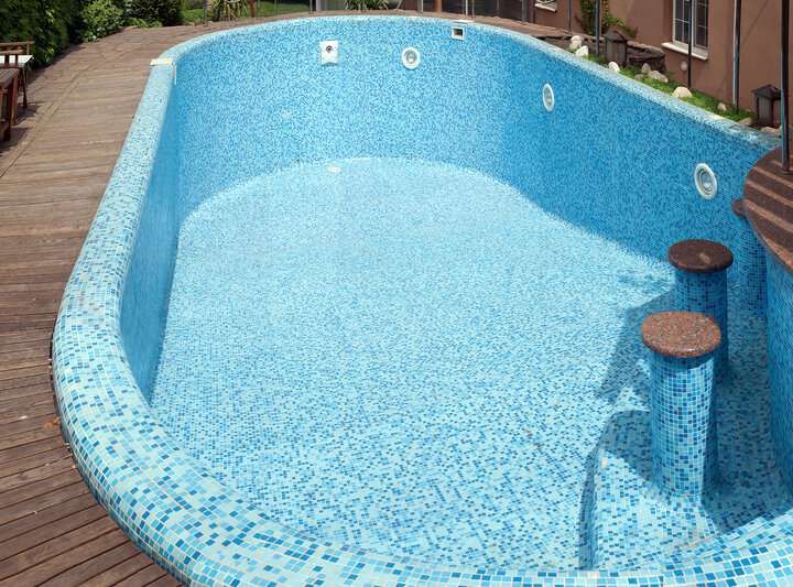 A sunny pool scene featuring a light blue tiled swimming pool with steps