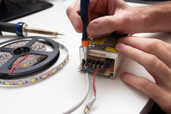 A person connecting wires to an LED driver while handling a soldering tool.