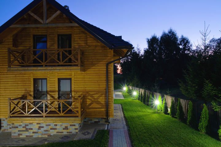 A wooden house at dusk with illuminated garden pathways and greenery.