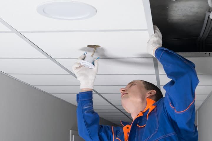 A technician installs LED lighting in a ceiling panel, focusing on the fixture.