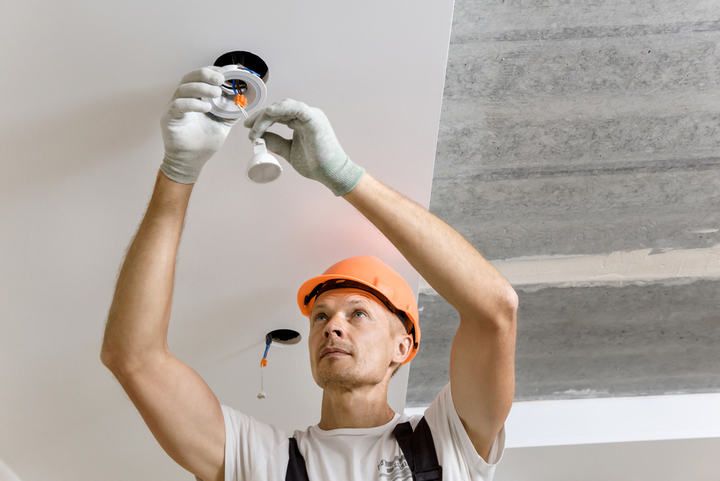 Worker installing LED ceiling lights with tools and safety gear.