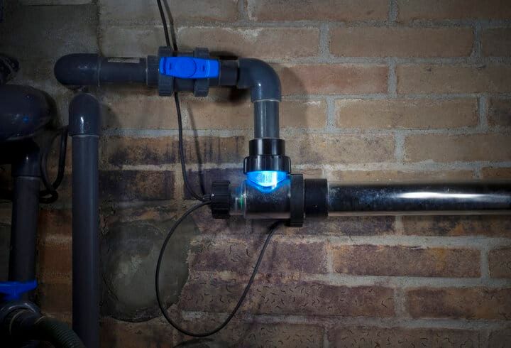 Close-up of blue LED light attached to dark plumbing pipes on a wall.