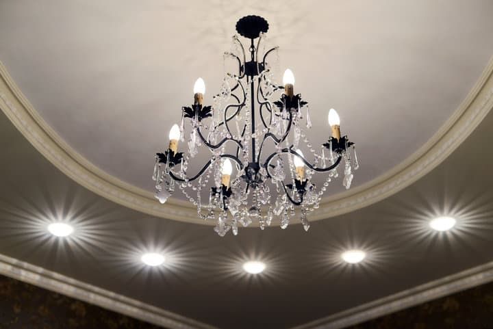 A decorative chandelier with eight lights surrounded by recessed lighting.