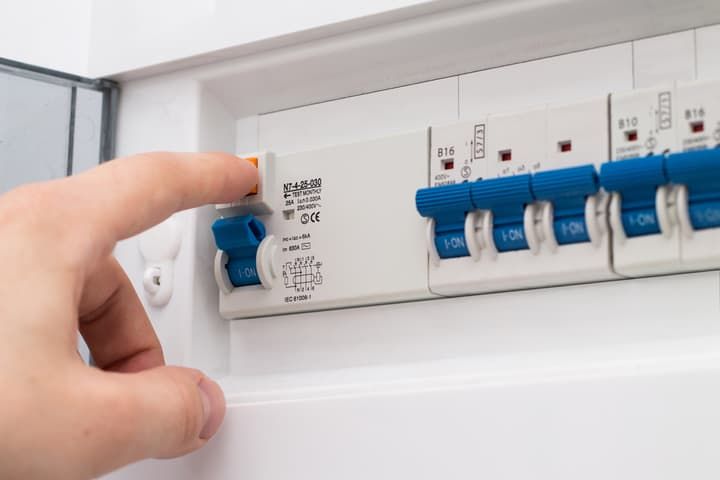 A hand is pressing a switch on an electrical circuit breaker panel.