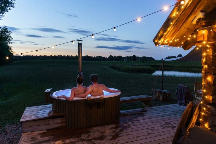 Couple relaxing in a hot tub under string lights at dusk.