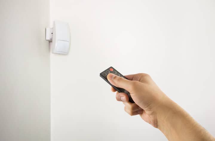 A hand holding a remote control pointing at a wall switch.