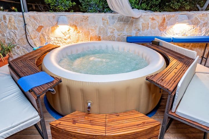 An inflatable hot tub surrounded by wooden seating and illuminated by soft LED lights.