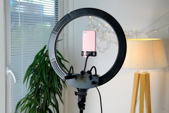 A ring light setup with a pink phone holder in a well-lit room.