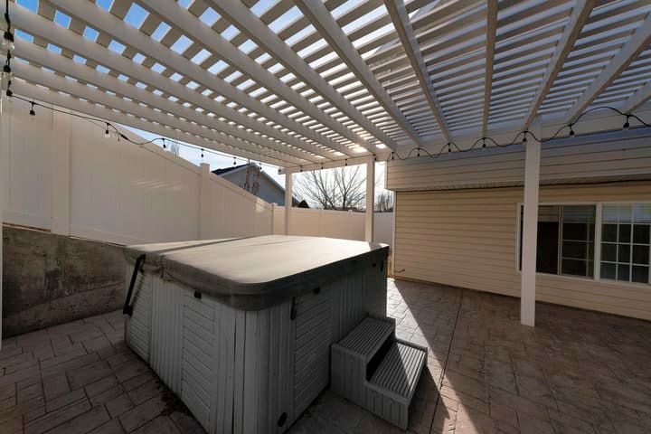 A spacious outdoor area featuring a hot tub under a slatted pergola.
