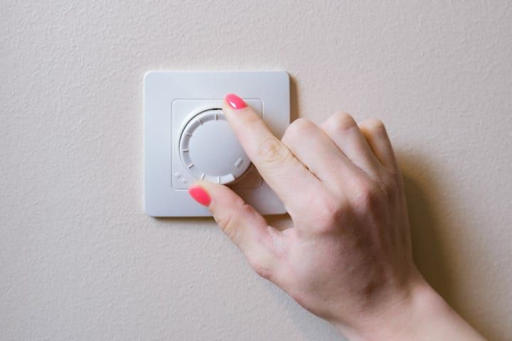 A hand adjusting a dimmer switch on a light control panel.
