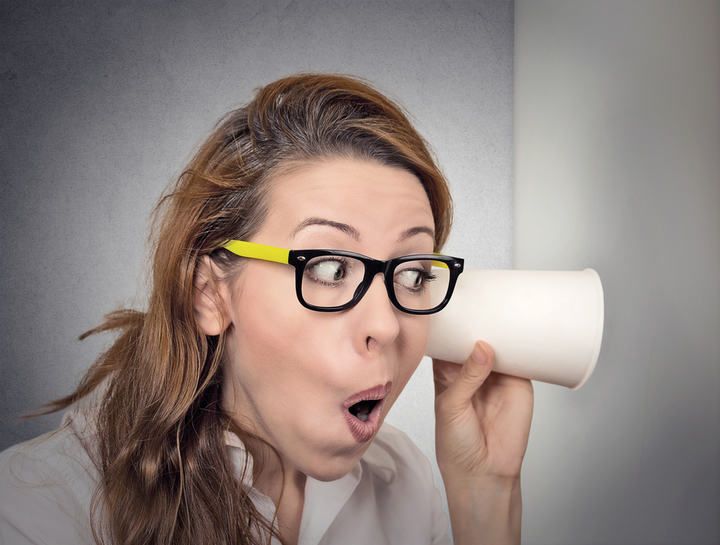 Woman with glasses listening intently to a cup, showing surprise.