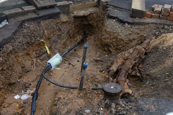 Excavated area showing exposed cables and rusted pipes in dirt.